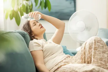 woman trying to stay cool with fan and water bottle