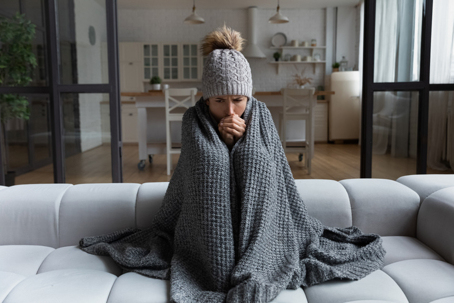 woman wearing a winter hat and wrapped in a blanket sits on a couch