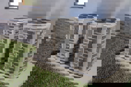 two modern AC condensers sitting on a concrete pad outside a home