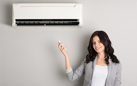 woman holding an AC remote control beside an AC unit